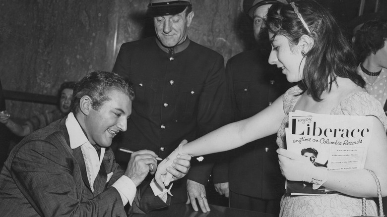 Liberace autographing a fan's glove, 1957